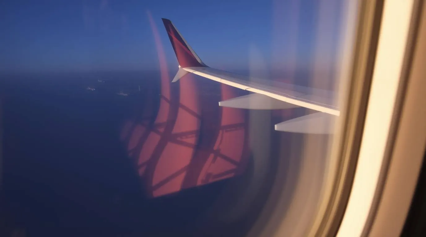 A view of an airplane wing seen through a passenger window above the ocean during daylight.